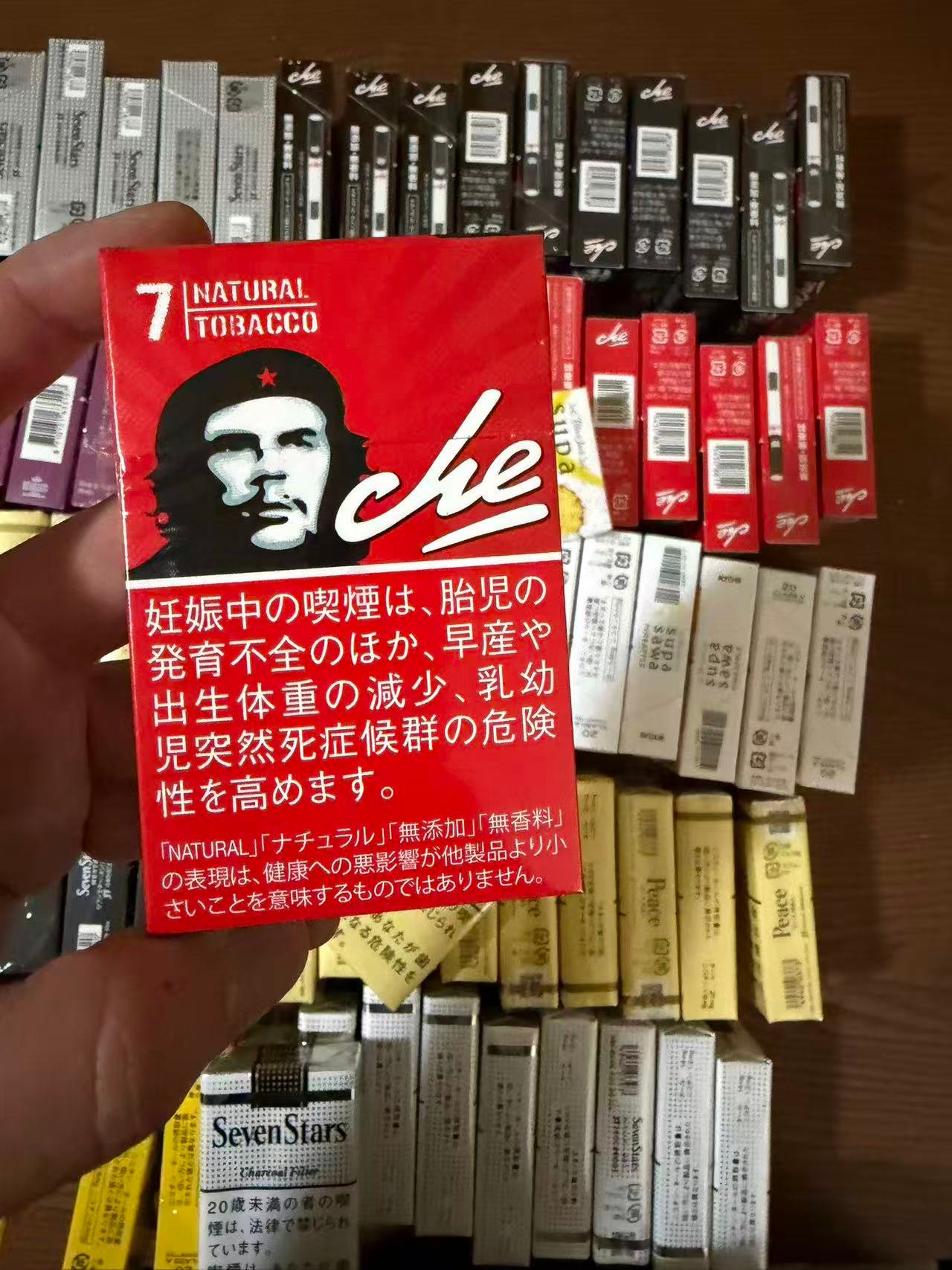 CHE LEADER 7mg pack held over a display of cigarette packs