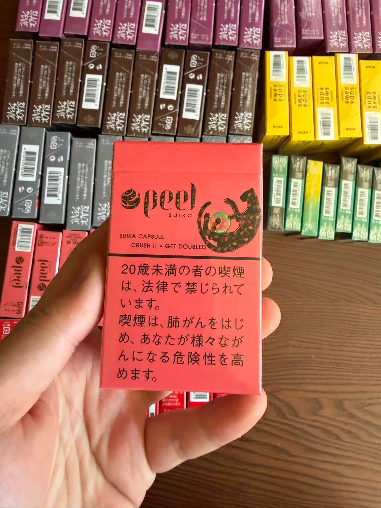 PEEL Suika Watermelon 9mg pack held over a display of cigarette packs