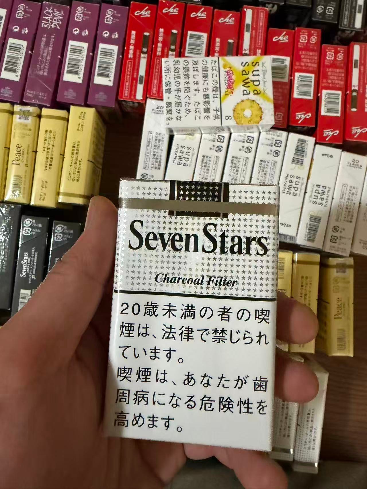 Seven Stars Charcoal Filter pack held over a display of cigarette packs