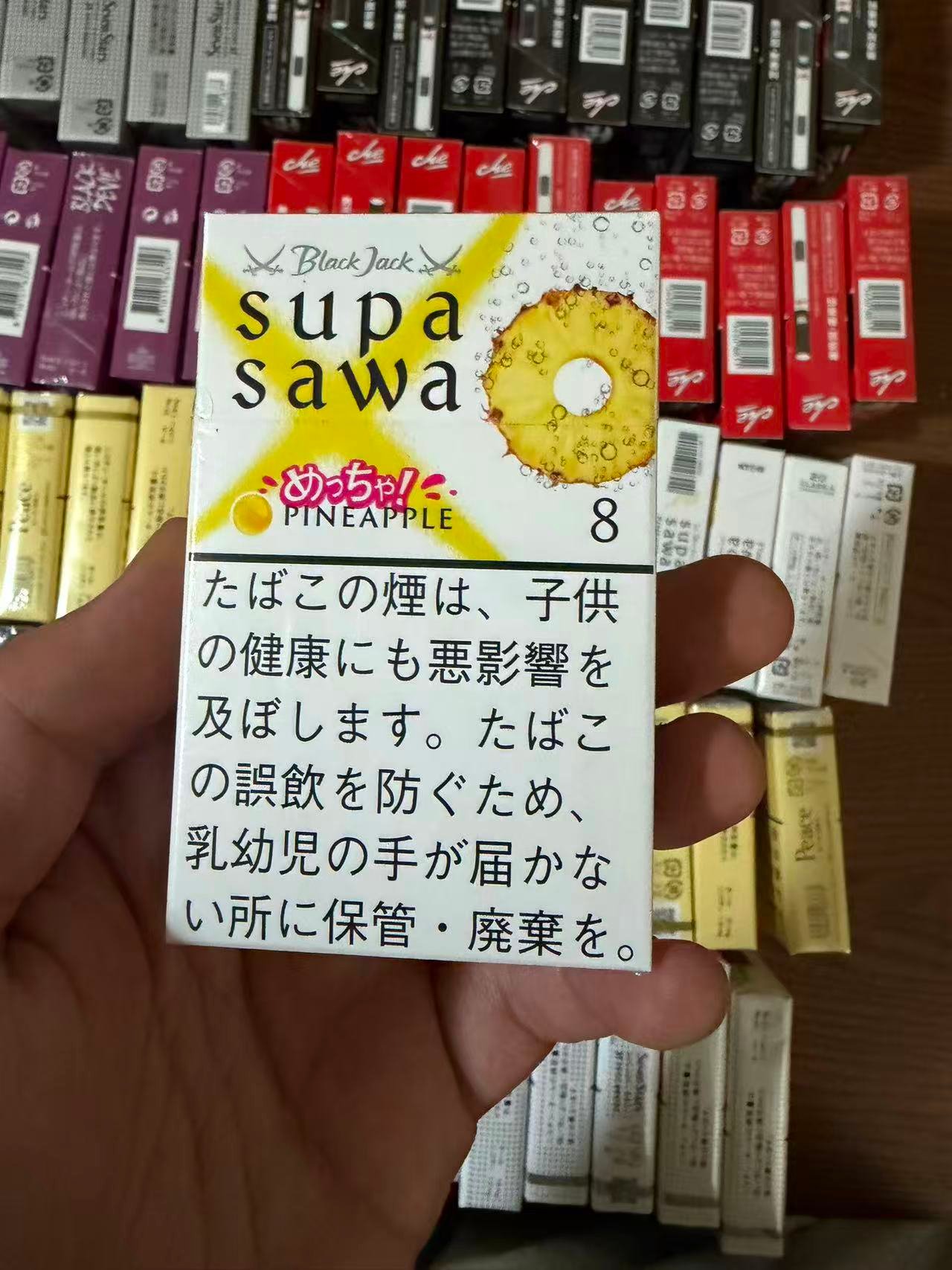 Supasawa Pineapple 8mg pack held over a display of cigarette packs